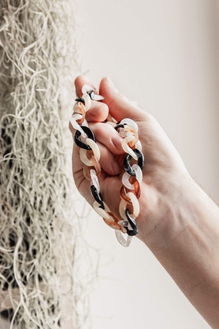 A hand holding links in front of a hanging plant.