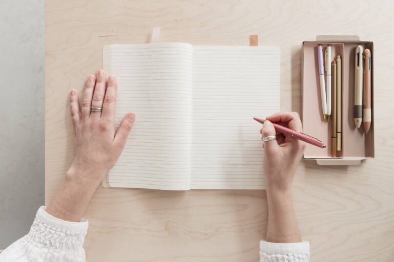 Hands holding a pen and opening a notebook with lined pages.